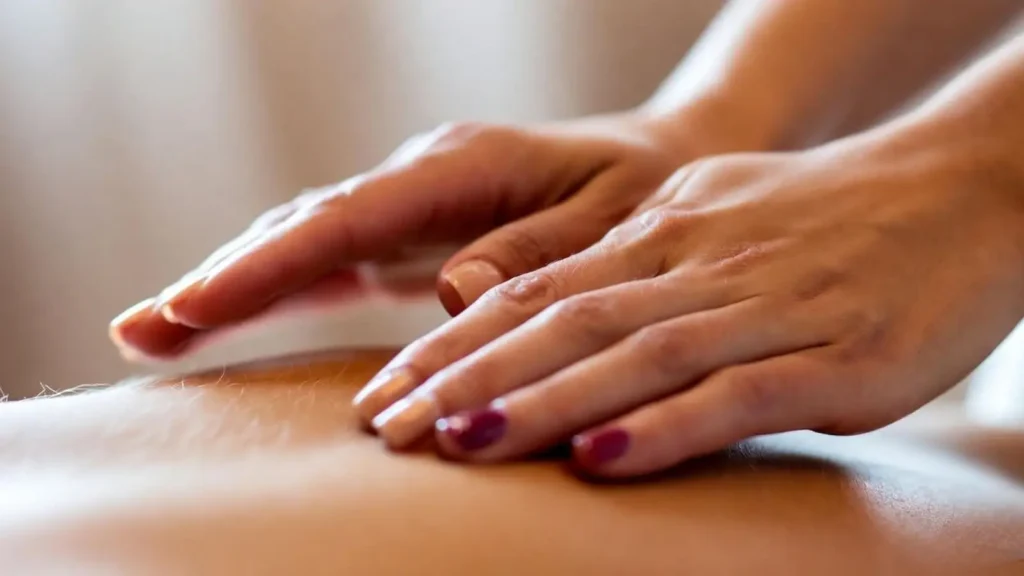 Mindful Touch – The Art of Connection Close-up of therapist’s hands hovering gently above a client’s back, warm neutral tones and motion blur suggesting rhythm and energy flow.
